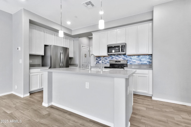 kitchen with sink, appliances with stainless steel finishes, an island with sink, pendant lighting, and white cabinets