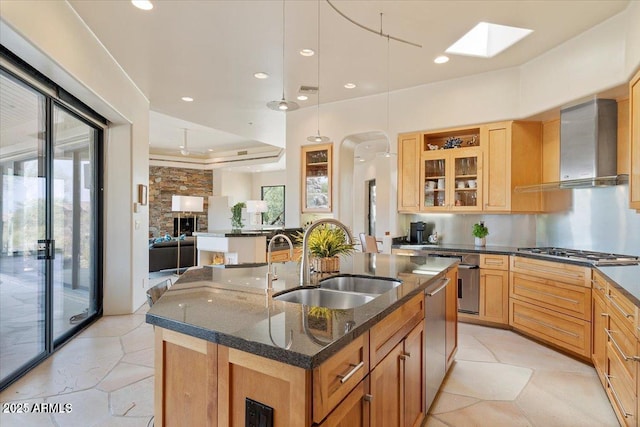 kitchen with wall chimney exhaust hood, sink, hanging light fixtures, an island with sink, and stainless steel appliances