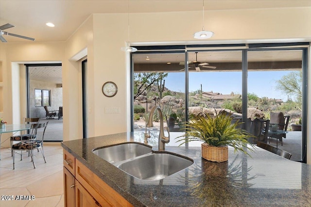 kitchen with dark stone countertops, sink, light tile patterned floors, and ceiling fan