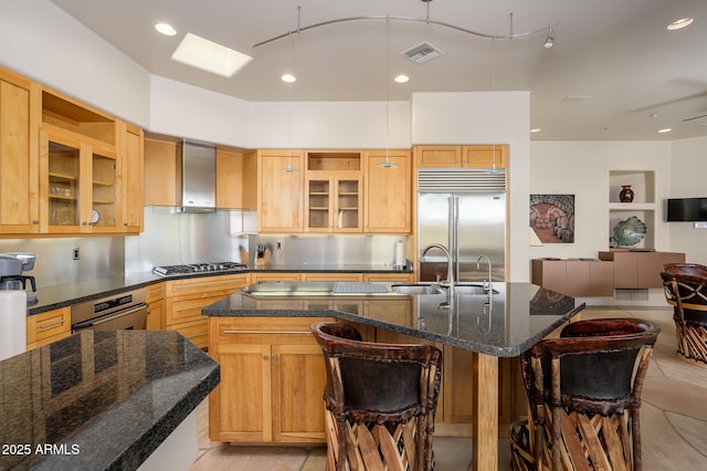 kitchen featuring wall chimney exhaust hood, a kitchen bar, sink, a center island with sink, and stainless steel appliances