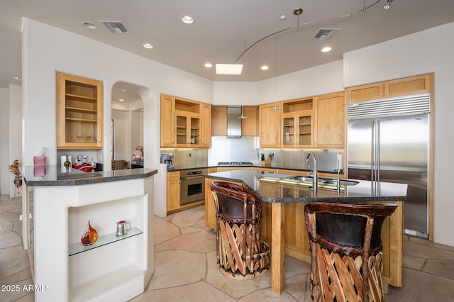 kitchen with appliances with stainless steel finishes, sink, a breakfast bar area, a center island with sink, and wall chimney exhaust hood