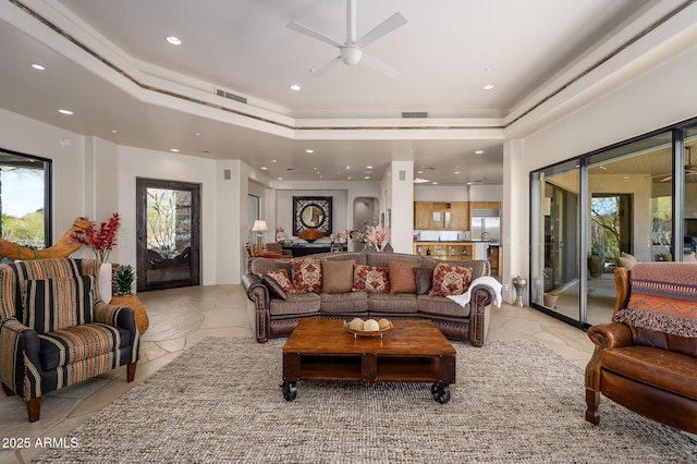 tiled living room with a raised ceiling and ceiling fan