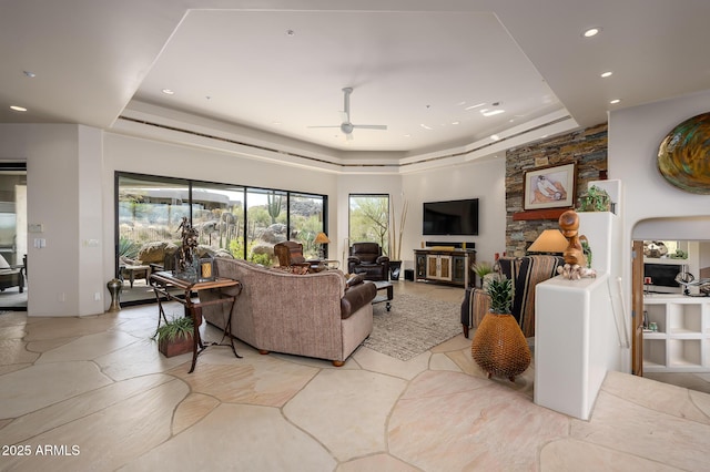 living room featuring ceiling fan, a tray ceiling, and a healthy amount of sunlight