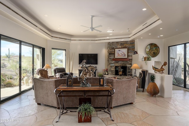 living room featuring ceiling fan, a fireplace, and a tray ceiling