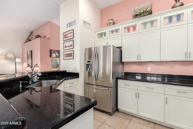 kitchen featuring light tile patterned flooring, sink, white cabinets, stainless steel fridge, and dark stone counters