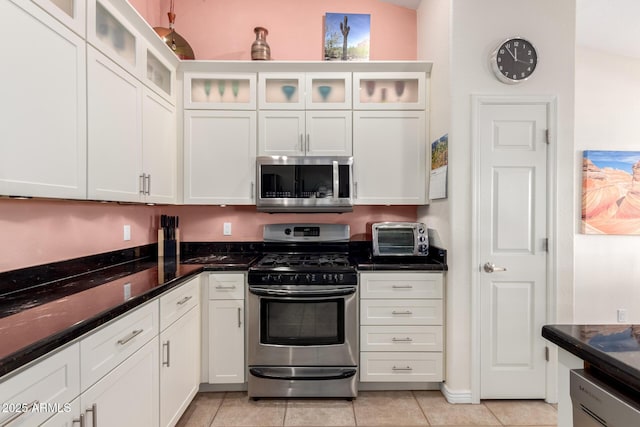 kitchen with white cabinetry, light tile patterned flooring, dark stone counters, and appliances with stainless steel finishes