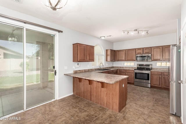 kitchen with a sink, a breakfast bar area, a peninsula, brown cabinets, and stainless steel appliances