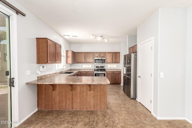 kitchen with a sink, a kitchen breakfast bar, a peninsula, brown cabinetry, and stainless steel appliances