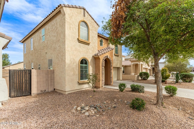 mediterranean / spanish-style house featuring stucco siding, a garage, fence, and a tiled roof