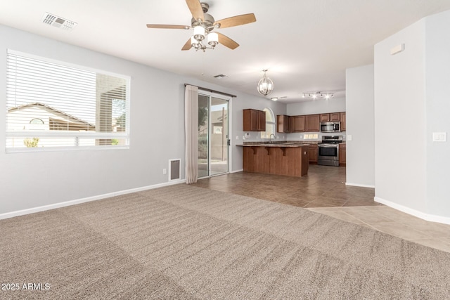 kitchen featuring a breakfast bar, ceiling fan with notable chandelier, open floor plan, stainless steel appliances, and light colored carpet