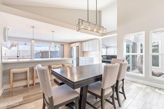 dining area featuring light wood-style flooring, high vaulted ceiling, and baseboards