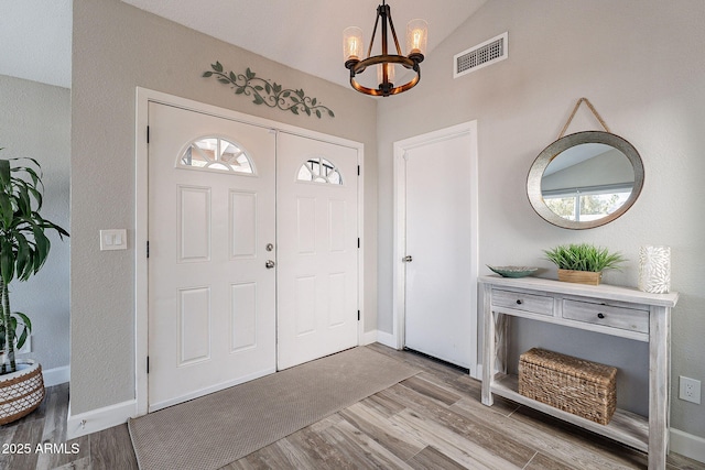 entrance foyer with visible vents, a notable chandelier, wood finished floors, baseboards, and lofted ceiling