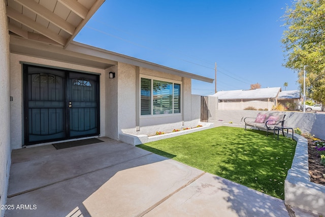 entrance to property with a lawn, fence, and stucco siding