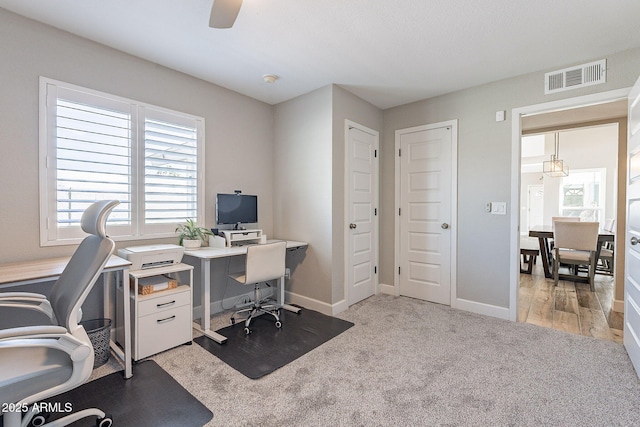 office space with visible vents, light carpet, baseboards, and a ceiling fan