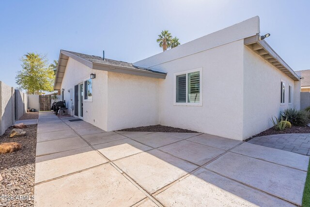 rear view of house featuring stucco siding, fence, and a patio area