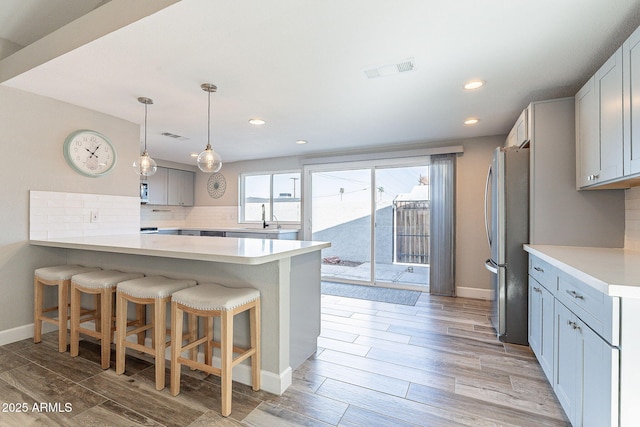 kitchen with visible vents, freestanding refrigerator, a sink, a kitchen bar, and backsplash