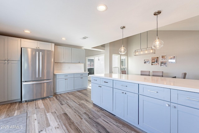 kitchen featuring tasteful backsplash, visible vents, light countertops, light wood-style flooring, and freestanding refrigerator