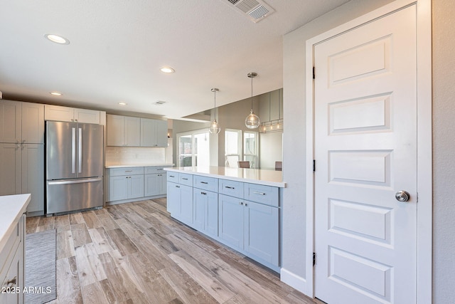 kitchen with visible vents, backsplash, freestanding refrigerator, light wood finished floors, and light countertops