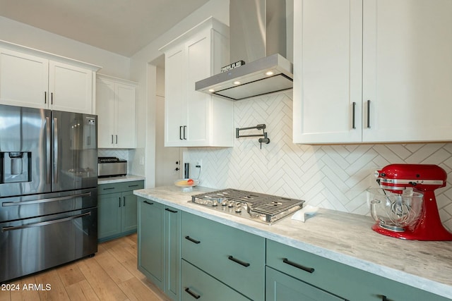 kitchen featuring backsplash, white cabinets, wall chimney range hood, light wood-type flooring, and stainless steel appliances