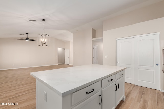 kitchen featuring light wood-type flooring, light stone counters, a kitchen island, white cabinetry, and decorative light fixtures