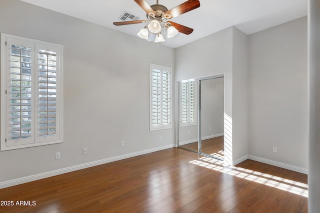 unfurnished bedroom with hardwood / wood-style floors, ceiling fan, a closet, and multiple windows