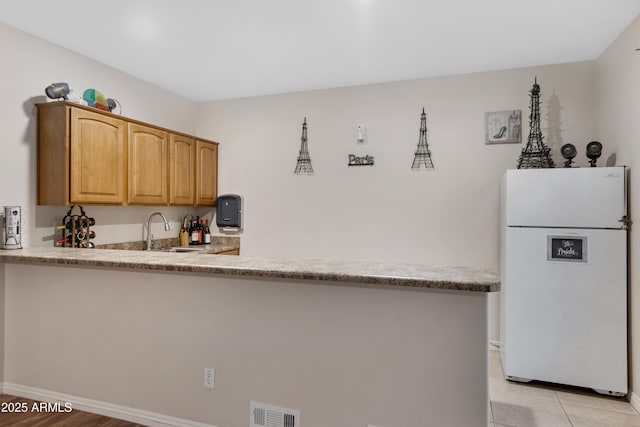 kitchen featuring sink, light tile patterned floors, white fridge, and kitchen peninsula