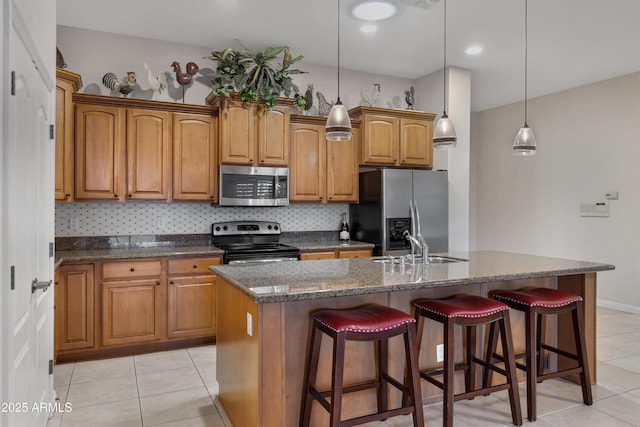 kitchen with appliances with stainless steel finishes, hanging light fixtures, an island with sink, decorative backsplash, and sink