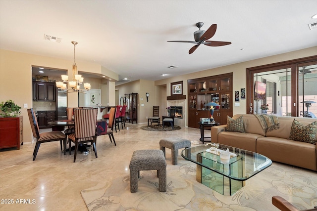 living area with a warm lit fireplace, visible vents, light tile patterned floors, and ceiling fan with notable chandelier