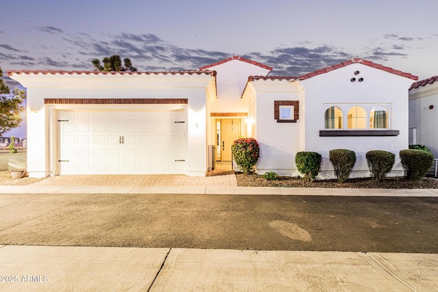 mediterranean / spanish-style house with an attached garage, a tile roof, decorative driveway, and stucco siding