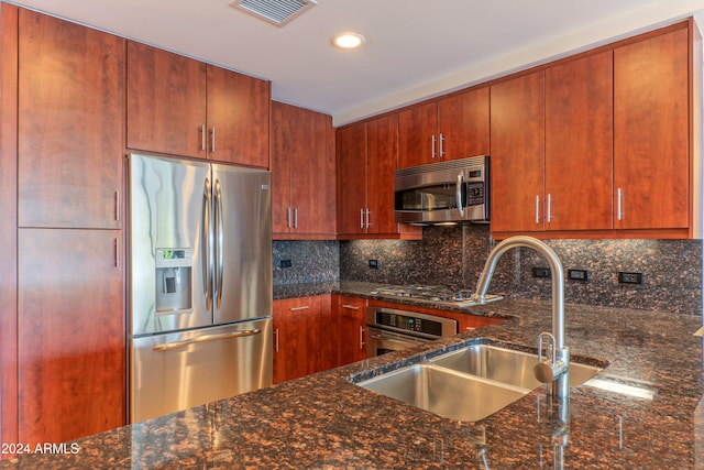 kitchen with backsplash, sink, stainless steel appliances, and dark stone countertops