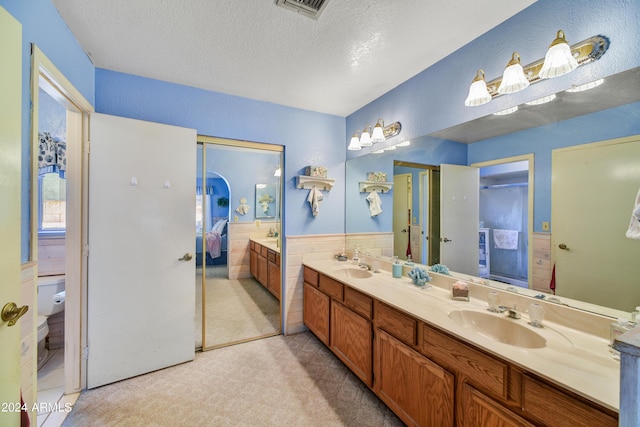 11630 N 74th Dr, Peoria, AZ 85345 - bathroom with toilet, a textured ceiling, a sink, double vanity, and wainscoting
