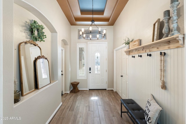 foyer entrance featuring arched walkways, a notable chandelier, a raised ceiling, wood finished floors, and baseboards