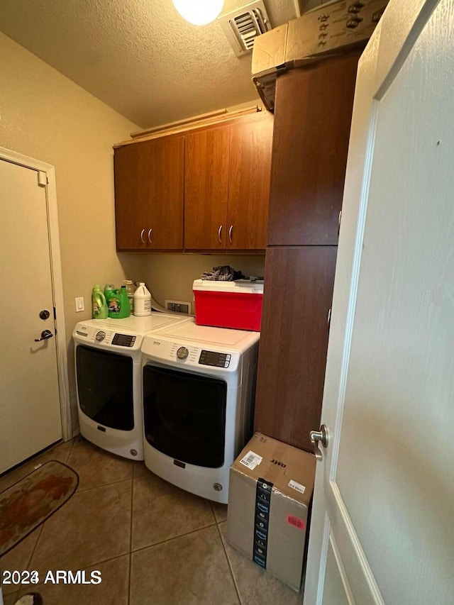 laundry room with light tile patterned floors, washer and clothes dryer, cabinets, and a textured ceiling