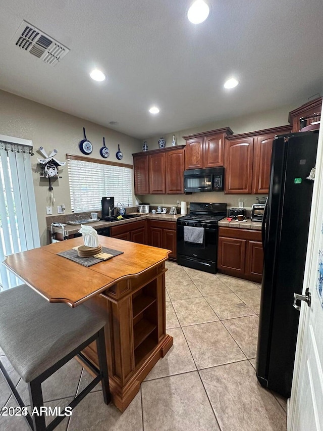 kitchen with a kitchen bar, sink, light tile patterned floors, and black appliances