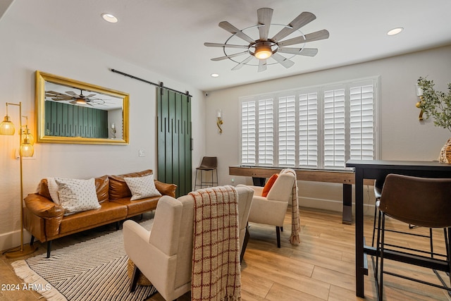 living room with light hardwood / wood-style floors, a barn door, and ceiling fan