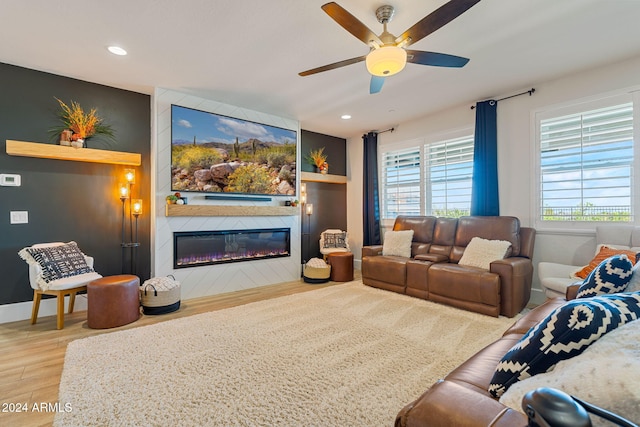 living room with light hardwood / wood-style floors, a large fireplace, and ceiling fan