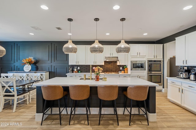 kitchen featuring hanging light fixtures, backsplash, a kitchen island with sink, light hardwood / wood-style floors, and stainless steel appliances