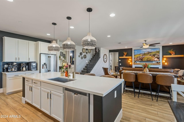 kitchen with white cabinets, appliances with stainless steel finishes, decorative light fixtures, and a kitchen island with sink