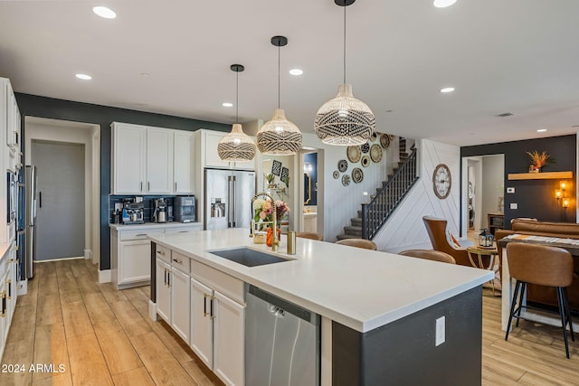 kitchen featuring white cabinets, stainless steel appliances, light wood-type flooring, and an island with sink