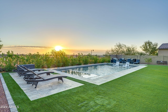 pool at dusk with a patio area and a lawn