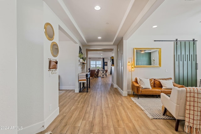 hallway featuring light hardwood / wood-style floors, a barn door, and a raised ceiling