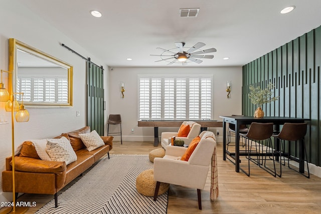 living room with a barn door, light wood-type flooring, and ceiling fan