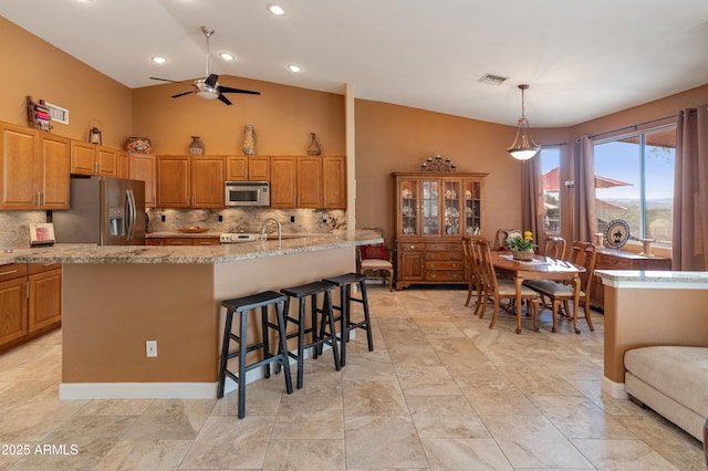43638 N 22nd St, New River, AZ 85087 - kitchen featuring appliances with stainless steel finishes, a ceiling fan, tasteful backsplash, light stone counters, and high vaulted ceiling