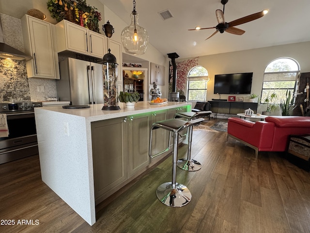 kitchen with a wood stove, a kitchen island, appliances with stainless steel finishes, wall chimney range hood, and pendant lighting