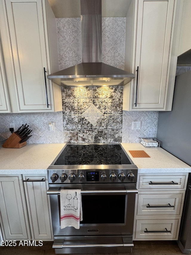 kitchen with high end stainless steel range, light stone countertops, wall chimney range hood, and backsplash