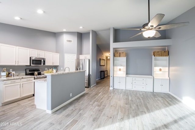 kitchen with white cabinetry, a kitchen island, stainless steel appliances, light stone countertops, and light hardwood / wood-style floors