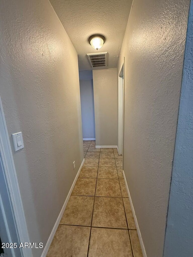 hall with light tile patterned floors, visible vents, a textured ceiling, and a textured wall