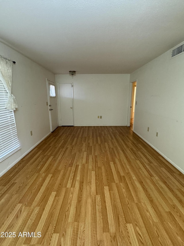 unfurnished living room featuring baseboards, visible vents, and light wood-style floors