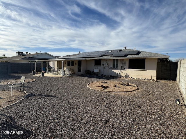 rear view of house with concrete block siding, a patio area, a fenced backyard, and solar panels