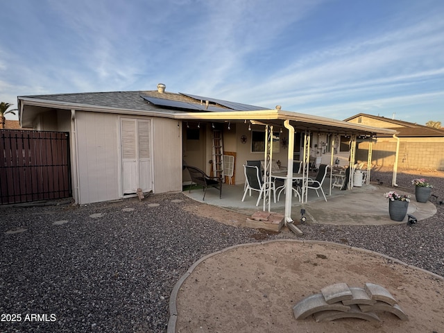 back of property with a fenced backyard, roof with shingles, solar panels, and a patio